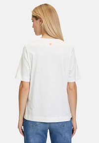 Hvid kortærmet t-shirt med lige snit og logo detalje på ryggen. Lavet af blød bomuld, har rund hals og afslappet pasform.