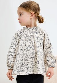 Long-sleeve blouse in cream fabric featuring black bow and floral patterns, gathered neckline, and elasticized cuffs.