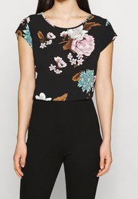 Blommig kortärmad topp i svart med blå, rosa och vita blommor; rund halsringning; lättviktigt tyg; matchad med svarta byxor.