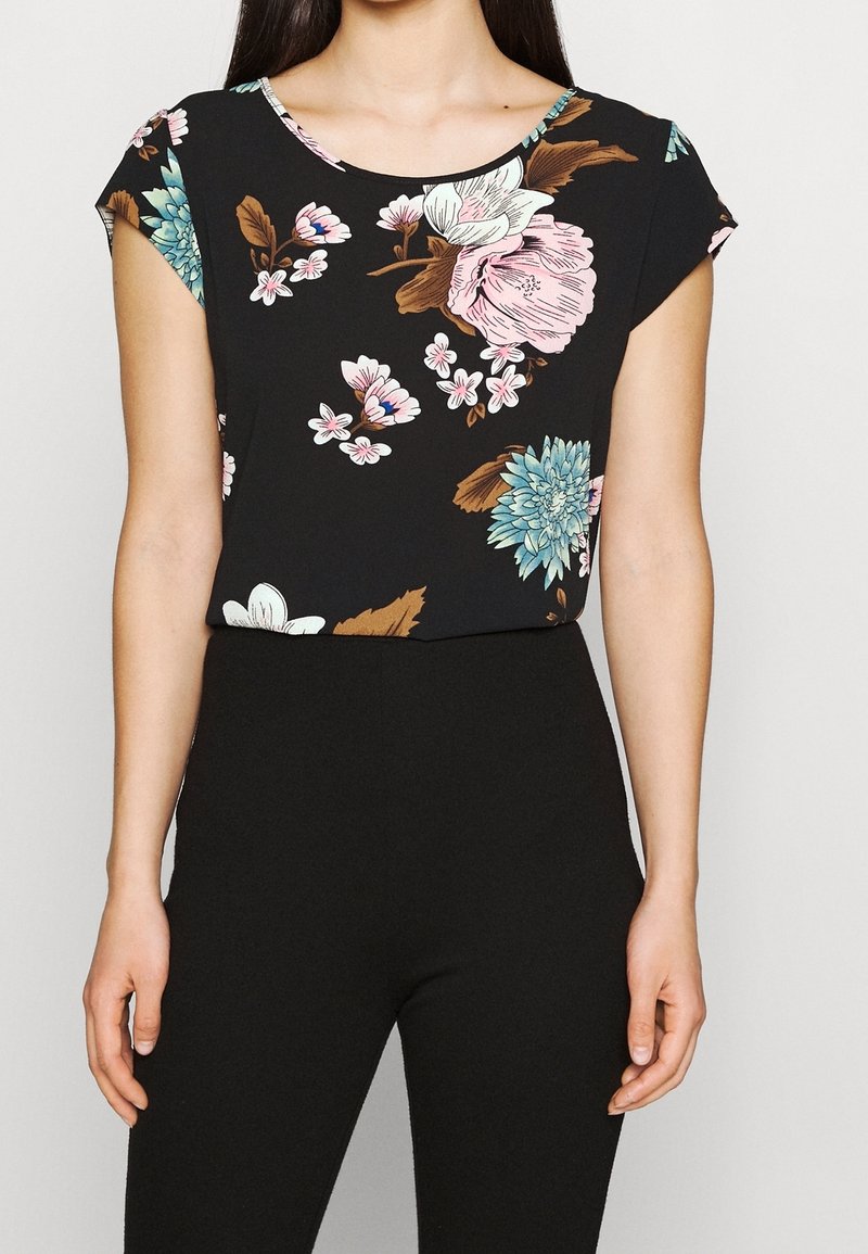 Blommig kortärmad topp i svart med blå, rosa och vita blommor; rund halsringning; lättviktigt tyg; matchad med svarta byxor.