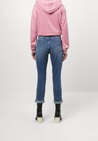 Sudadera rosa claro con cordón, combinada con jeans de tiro alto azul medio. Los jeans tienen puños enrollados y dos bolsillos traseros. Botines negros de tacón.