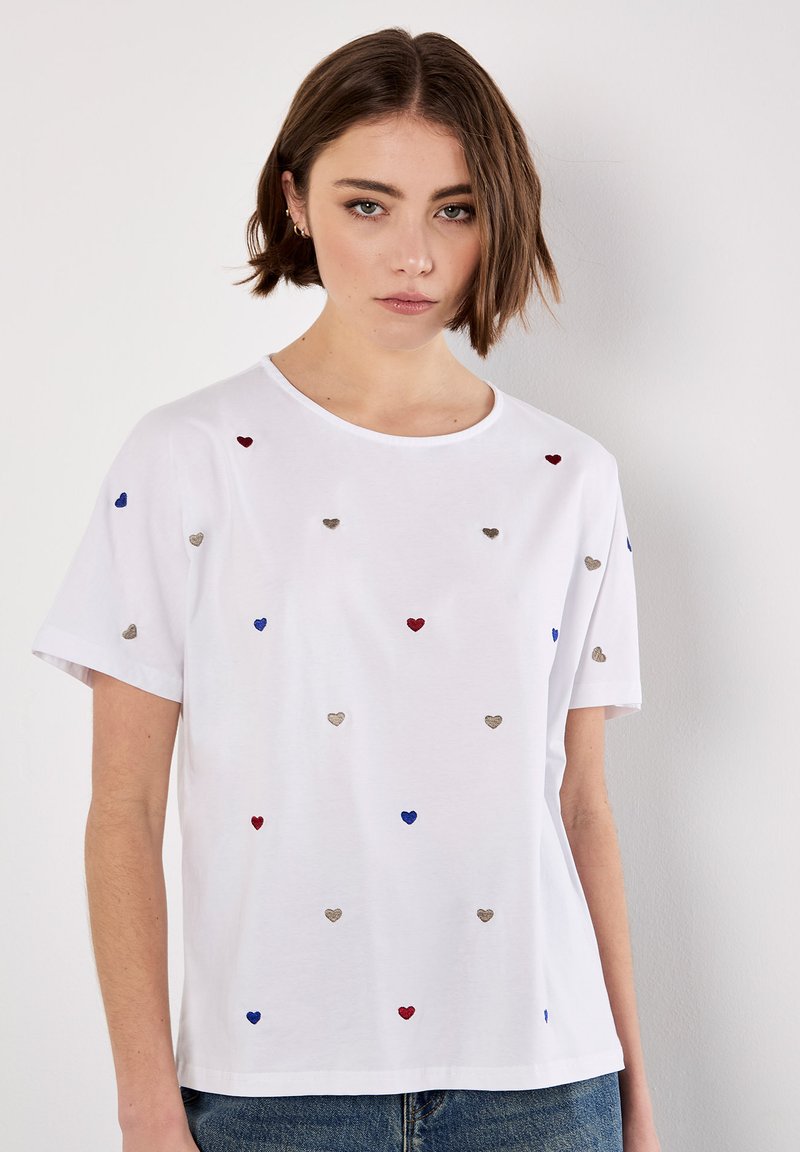 Hvid kortærmet t-shirt med spredte broderede hjerter i rød, blå og sølv. Rund halsudskæring med en afslappet pasform.