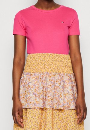 Persoon draagt een roze T-shirt met korte mouwen gecombineerd met een gele, hoog getailleerde rok met een gelaagd bloemmotief.