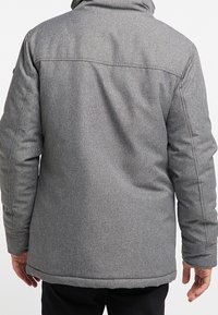 Giacca isolante grigia con finitura tessile liscia, dotata di cappuccio, maniche lunghe e un taglio dritto. Cuciture visibili sul retro.