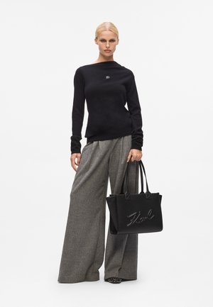 Maglione nero a maglia con scollo rotondo, pantaloni grigi a gamba larga e una borsa a tracolla nera con texture che mostra la scritta "Karl" in rilievo.