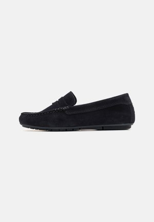 Black suede loafers with a rounded toe, visible stitching, and a decorative strap across the front. Matte black rubber sole for traction.