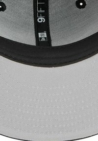 Graue Kappe mit flachem Schirm, schwarzen Akzenten und strukturiertem Stoff. Innen befindet sich ein Etikett mit Größen- und Markenangabe.