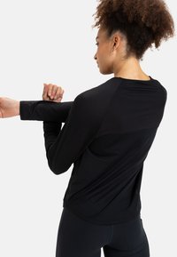 Mustapohjainen urheilupaita pitkällä hihalla, jossa on pyöreä kaulus ja sileä rakenne, raglan-hihat sekä kaareva helma.