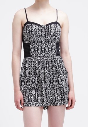Femme portant une combinaison sans manches noire et blanche à motifs avec des fines bretelles et un corsage ajusté.