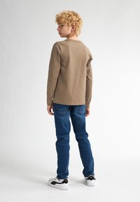 Camicia marrone a maniche lunghe abbinata a jeans in denim blu e sneakers bianche. La camicia ha un col girocollo e una vestibilità comoda.