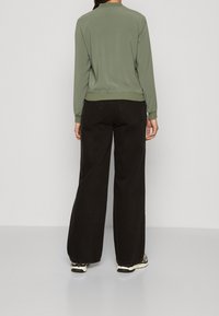 Lös passform i olivgrön jacka med ribbat avslut och ärmar, tillsammans med svart byxor med hög midja och vida ben. Enkel design, minimala detaljer.