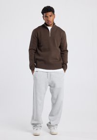 Brown zip-neck sweater with a relaxed fit, paired with light grey sweatpants. Sweatshirt features ribbed cuffs and waistband.