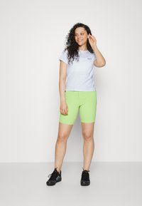 Light gray cotton t-shirt with a round neck, paired with bright green bike shorts. Model wears black athletic shoes. Simple design, no patterns.