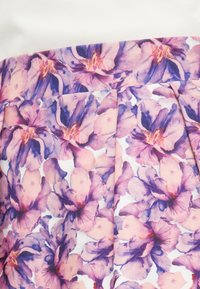 Ύφασμα με μεγάλο ροζ και μοβ φλοράλ σχέδιο που απεικονίζει λουλούδια που μοιάζουν με ορχιδέες σε λευκό φόντο με ορατές ραφές και πιέτες.