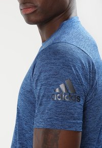 Blå heathered tränings t-shirt med korta ärmar, som har en svart Adidas-logotyp på vänster axel. Tillverkad av ett mjukt, strukturerat tyg.