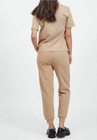 Jasnobrązowa, krótki rękaw koszulka i pasujące dresy wykonane z miękkiego materiału, z elastycznymi mankietami, noszone z czarnymi butami.