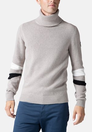 Jersey de cuello alto de color gris claro con ribete en el cuello y los puños. Presenta franjas blancas y negras contrastantes en las mangas, confeccionado en tejido de punto.