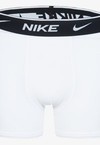 Bela bombažna boksarica z črnim gumiranim pasom, na katerem je bel logotip "NIKE". Gladka tekstura, prilegajoča zasnova z dolžino do sredine stegna.