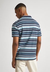 Svītrains polo krekls ar tumši zilo, gaiši zilo un baltu krāsu toņiem. Īsas piedurknes, apkakle un teksturēta auduma materiāls ar brīvu piegriezumu.