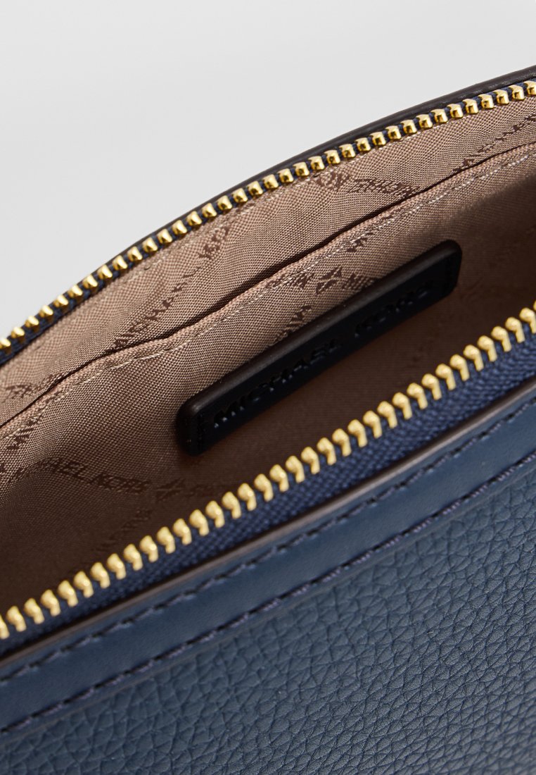 Intérieur d'un sac en cuir bleu marine avec une doublure brun clair, doté d'une fermeture éclair dorée et d'une étiquette noire embossée du nom de la marque.