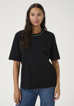 Sort bomulds T-shirt med korte ærmer og rund halsudskæring, der har en subtil metallisk detalje ved kraven, kombineret med blå denim jeans.
