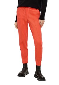 Helle korallenfarbene Hosen aus glattem Stoff, ausgestattet mit einem Kordelzugbund, einem taillierten Bein-Design und vertikalen Nähdetails. Kombiniert mit schwarzen Stiefeln.
