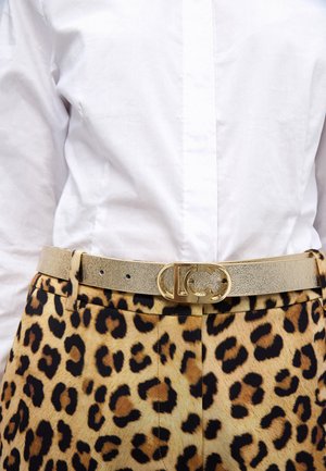 Cinturón metálico dorado con acabado texturizado y hebilla circular, usado sobre pantalones con estampado de leopardo, combinado con una camisa blanca lisa.