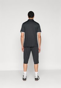 Σκούρο γκρι αθλητική στολή που περιλαμβάνει πόλο με κοντό μανίκι και σορτς μήκους μέχρι το γόνατο, και τα δύο με λευκή επένδυση, συνδυασμένα με αθλητικά παπούτσια σε μαύρο και άσπρο χρώμα.