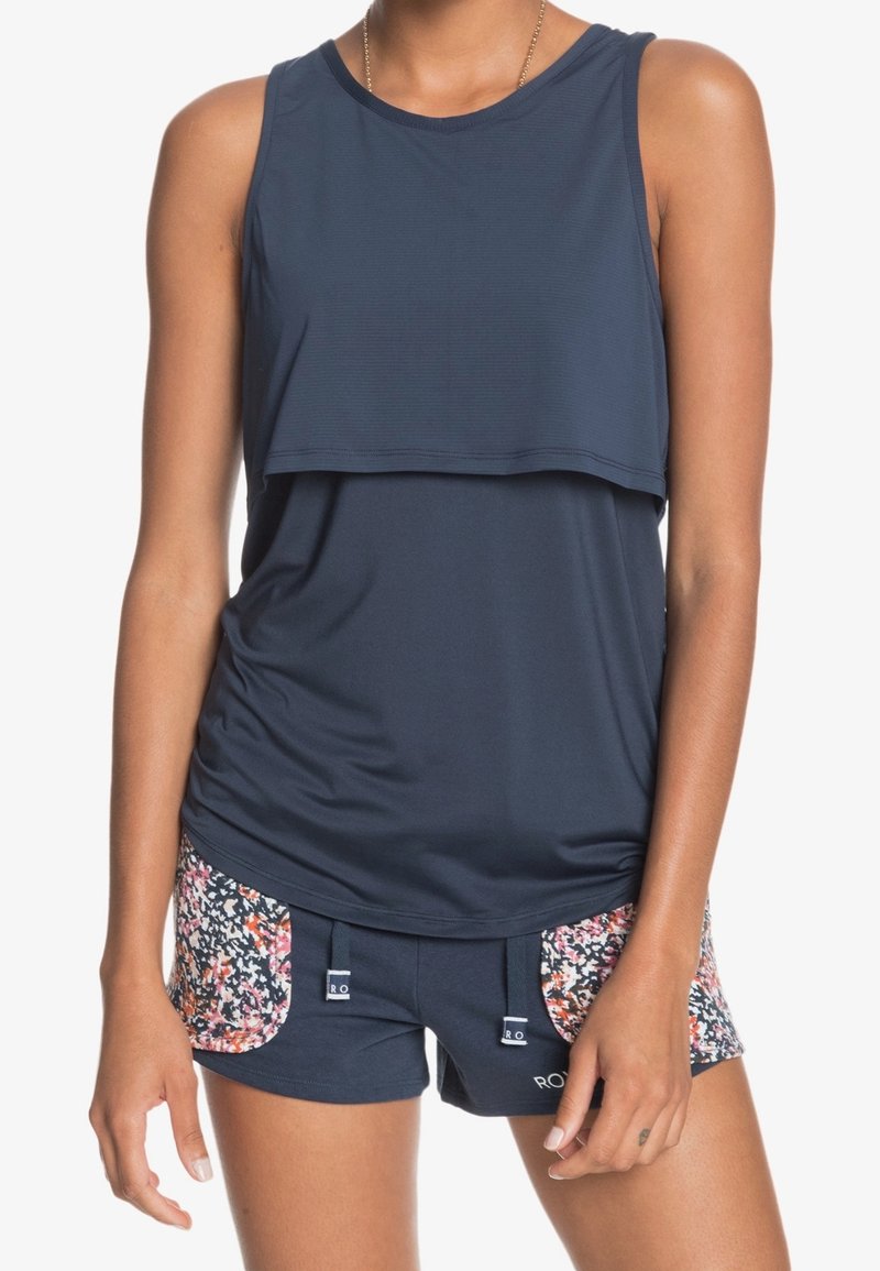 Mörkblå idrottstopp med lagerdesign; matchad med mörkblå shorts med blommönstrade sidofickor och dragsnörningsdetaljer.