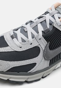 Nike sportbačiai, turintys mišrią audinio konstrukciją iš juodo tinklo ir pilkos zomšinės medžiagos, su pilkomis raišteliais, ryškiai išreikštu swoosh logotipu ir tekstūruotais akcentais.
