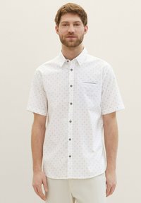 Camicia bianca a maniche corte con un sottile motivo geometrico, dotata di una tasca sul petto e bottoni scuri per creare contrasto.
