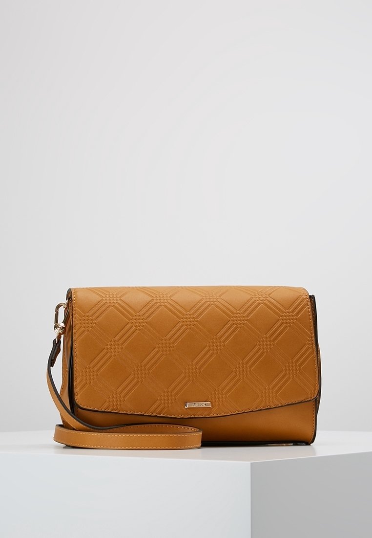 Sac bandoulière beige avec un motif losanges texturé et une sangle réglable, posé sur une surface blanche sur fond uni.