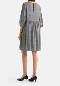 Černobílé šaty s puntíky, krátkými nabíranými rukávy, výstřihem vzadu ve tvaru klíče a nařaseným pasem, doplněné černými lodičkami na špic.