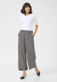 Black and white patterned wide-leg trousers with an elastic waistband and pockets, paired with a fitted white top and black heels.