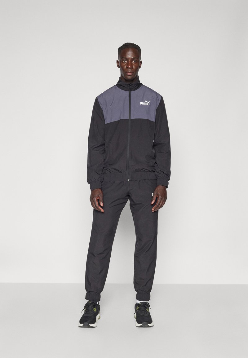 Schwarzer und grauer Trainingsanzug, mit Reißverschluss versehenen Jacke mit elastischen Bündchen und Hose mit Knöchelabschlüssen, jeweils mit weißem Puma-Logo.