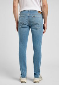 Jeans de denim azul claro con corte slim, que presentan dos bolsillos traseros, costuras sutiles y un parche de cuero de la marca en la cinturilla.