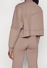 Sweatshirt court Nike en taupe clair, avec un grand logo ton sur ton dans le dos, des poignets côtelés et une texture douce et lisse.
