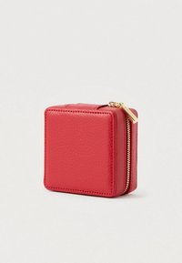 Kompakt négyzet alakú vörös bőrpénztárca, textúrázott felülettel és arany cipzárral, fehér háttér előtt bemutatva.