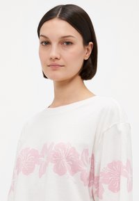 Witte katoenen t-shirt met een roze bloemenpatroon aan de onderkant. Casual, relaxte pasvorm met brede mouwen en een zachte textuur.