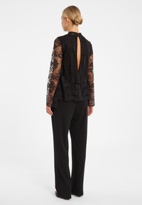 Zwarte kanttop met lange mouwen en een sleutelgatopening aan de achterkant, gecombineerd met zwarte broeken voor een strakke, gelaagde look.