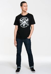 Black graphic t-shirt with white skull and crossbones design, featuring the words "Redwood Original SAMCRO Established 1967." Worn with dark denim jeans.