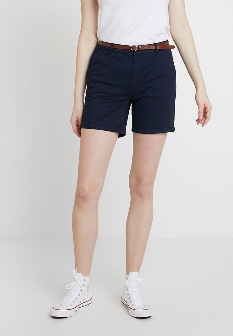 Mörkblå shorts med slim fit, upprullad fåll och ett brunt bälte. Kombineras med vita hög-top sneakers och en enkel vit t-shirt.