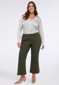 Camicia lunga in satin grigio chiaro con chiusura a bottoni abbinata a pantaloni a gamba larga verde oliva e scarpe con tacco a fantasia.