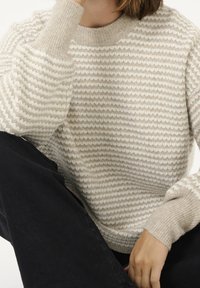 Sweter dziergany w kremowym i jasnobeżowym kolorze z teksturowanymi paskami. Z okrągłym dekoltem i ściągaczami przy mankietach, wykonany z miękkiego materiału.