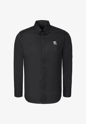 Camicia nera a maniche lunghe con bottoni e colletto abbottonato, con un piccolo logo bianco sul petto raffigurante un volto stilizzato con occhiali da sole.