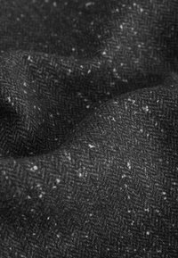 Tăietură cu model houndstooth în negru, cu pete gri și albe, realizată dintr-un amestec de lână brută, având o suprafață moale și texturată.