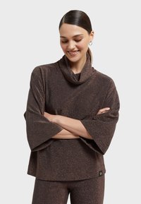 Brauner, glitzernder Cowl-Nek-Top mit breiten Ärmeln, das eine strukturierte Oberfläche aufweist. Beinhaltet ein kleines Logotag auf der unteren linken Seite.