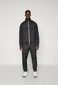 Musthave musta sportlik jope täispika tõmbluku ja valge aktsendiga, paaris sobivate mustade pükstega. Mõlemad on valmistatud siledast, kergest materjalist.