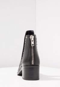 Black leather ankle boot with silver zipper on back and silver studs along sides, featuring a low stacked heel.