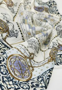Zijde sjaal met sterrenbeelden, astrologische symbolen en sierlijke gouden ketens op een witte en blauwe bloementextuur.